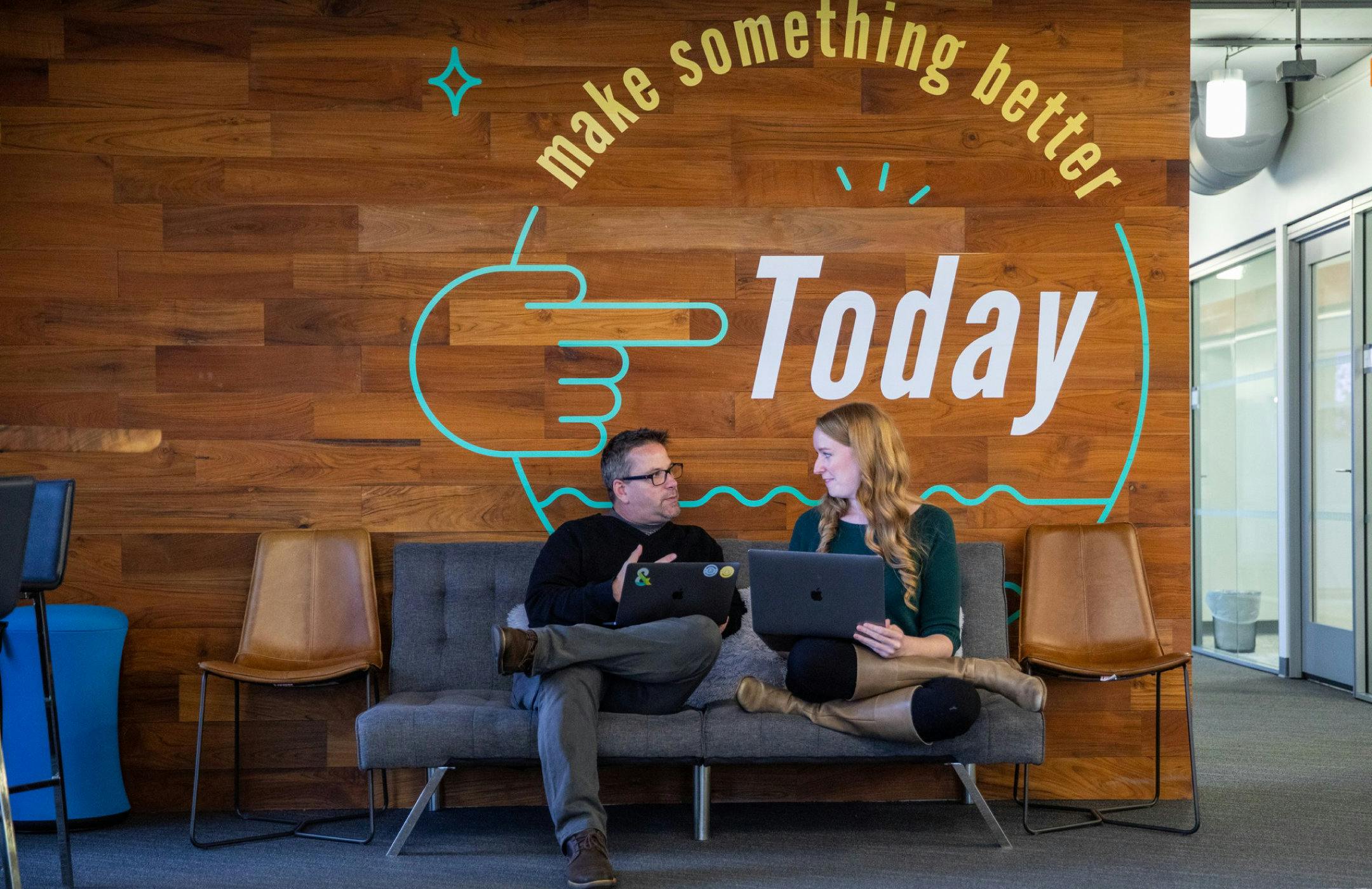 Photo of two Amperity employees collaborating under a sign that says "Make something better today"